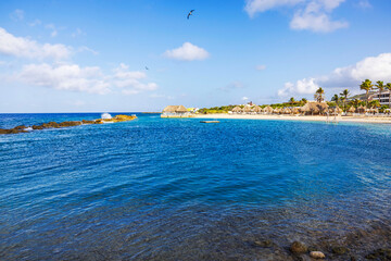 Obraz premium Beautiful tropical beach with clear blue water, palm trees, and thatched huts on Curacao island.