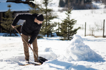 Man cleaning snow in the yard, collecting it to make a snowman