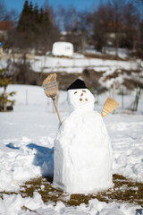 White snowman in the yard with brooms as arms