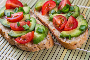 Avocado toast topped with tomato and green onion on a slice of carrot bread