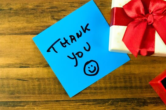 A paper with a thank you note on it. The note was written in black marker and next to a gift box with a ribbon.