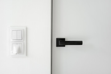 Modern black door handle and white light switch on wall