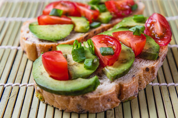 Avocado toast topped with tomato and green onion on a slice of carrot bread