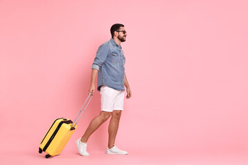 Happy man in sunglasses with suitcase on pink background