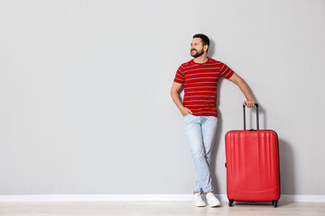 Happy man with suitcase near light gray wall indoors, space for text