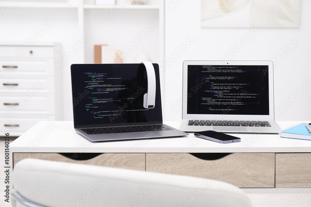 Poster programmer's workplace. modern laptops with unfinished code, headphones and smartphone on desk indoo