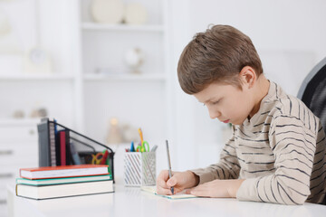 Boy with incorrect posture doing homework at white desk indoors