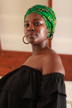 African woman wearing a green doek head wrap with blue denim jeans and black top