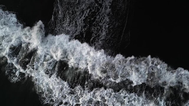Dramatic aerial top view of ocean waves breaking on black volcanic shore. Water motion, white waves and dark sand