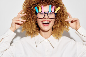 Smiling woman with curly hair and colorful clips in glasses on a bright white background,...