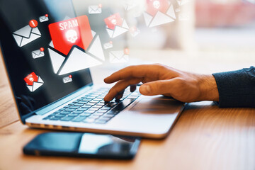 Hand typing on laptop with spam email notifications.