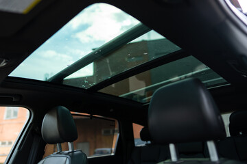 Polarised sunroof of luxurious automobile with urban sky scenery shot from inside of vehicle. Glass...