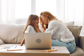 Mother and daughter bonding time on the couch, exploring educational content on a laptop together in a cozy living room