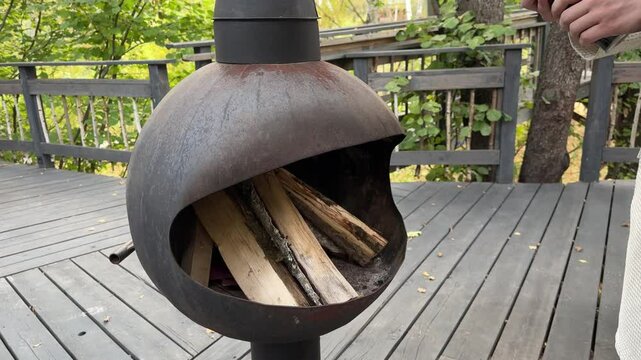 A man starts a fire in a backyard fireplace using kindling - lighting a gas cylinder, gas burner, surrounded by beautiful fall foliage on a sunny day.