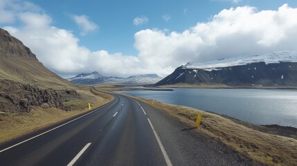 An empty highway in Iceland, with precise road markings, winding through scenic lakes and mountains under a bright, cloud-filled sky.