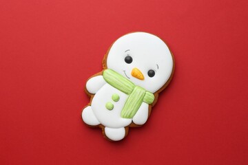Tasty Christmas cookie in shape of snowman on red background, top view
