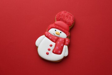 Tasty Christmas cookie in shape of snowman on red background, top view