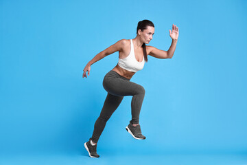 Fototapeta premium Woman in sportswear running on light blue background