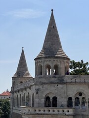 A stunning view of the Fisherman's Bastion in Budapest, showcasing its unique architectural towers, intricate stonework, and a bright blue sky dotted with fluffy clouds. Ideal for travel themes.
