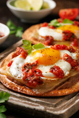 Huevos Rancheros tostadas with fried egg, tomato salsa, bean paste and cheese on wooden board