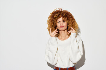 Young woman with curly hair making a playful gesture against a plain white background, wearing a cozy sweater, embodying a fun and quirky vibe