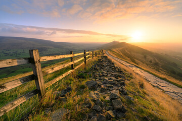 Golden sunrise at Mam Tor with footpath leading along ridge in The Peak District, UK.