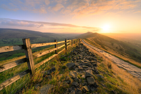 Golden sunrise at Mam Tor with footpath leading along ridge in The Peak District, UK.