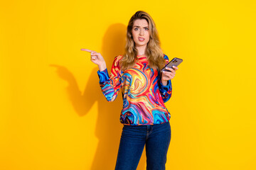 Photo of lovely young lady point disgusted empty space hold device dressed stylish colorful garment...