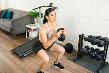 Determined young woman performs squats while using a kettlebell in her home workout routine