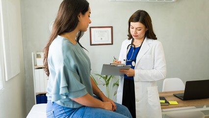 Female doctor attentively listens to her patient and jots down notes on a clipboard during a...