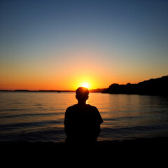 Person sitting by a lake at sunset