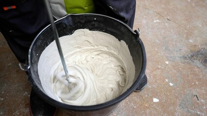 Construction worker mixing cement in a bucket using an electric mixer.