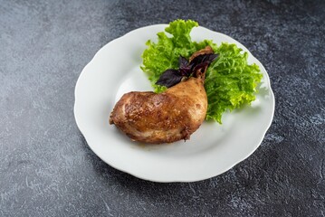 A piece of meat is on a white plate with green lettuce
