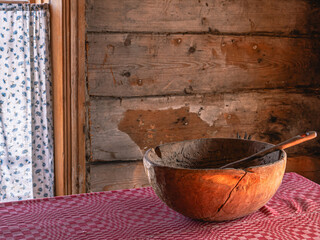 In a rustic house in the kitchen, there is an old wooden bowl with a spoon on the table. The interior of the kitchen of a rural house built in the 19th century. A red tablecloth on an antique table.