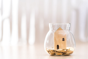Wooden house model put on the bottle with gold coin inside in the office, Saving money or loan for business investment real estate or buy a new home for a family concept.