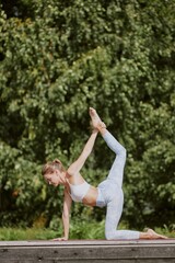 Vertical shot of young shredded woman in fashionable sportswear stretching her all body muscles on mat