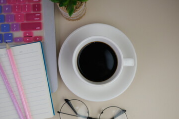 Flatlay of coffee with pink office tools, pink headphone, notebook, pen and a bouquet of pink tulips on pink background as copy space concept