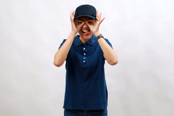 Young hispanic woman courier wearing delivery uniform and cap doing ok gesture like binoculars sticking tongue out, eyes looking through fingers. crazy expression.