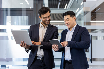 Two male professionals in business attire discussing project details using laptop and tablet....