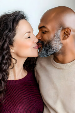 A senior interracial couple, an African man and a Caucasian woman, share a loving kiss at home, expressing deep affection.