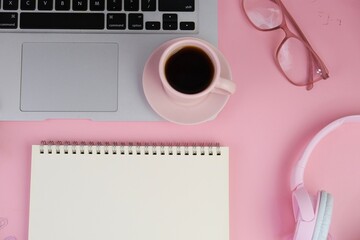 Flatlay of coffee with pink office tools, pink headphone, notebook, pen and a bouquet of pink tulips on pink background as copy space concept