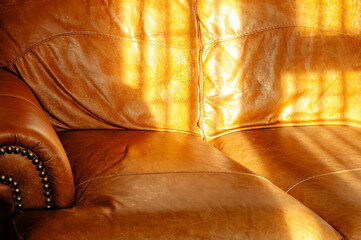 Close up of a leather sofa seen in strong daylight, the window light creating shadows on the...
