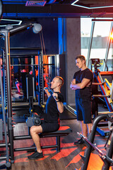 Man performing lat pulldown exercise in modern gym. A man completes a lat pulldown while a trainer supervises in a vibrant, well-lit gym setting during the evening.