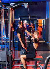 Two men working out with gym equipment together. A fitness trainer assists a client with cable...
