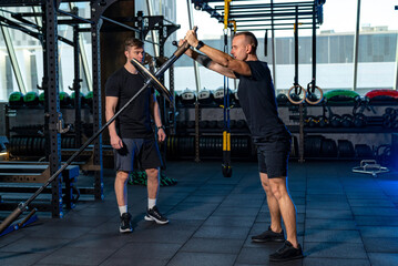 Trainer leads session in modern gym. A personal trainer assists a client with an exercise using a training bar in a contemporary gym during a training session.