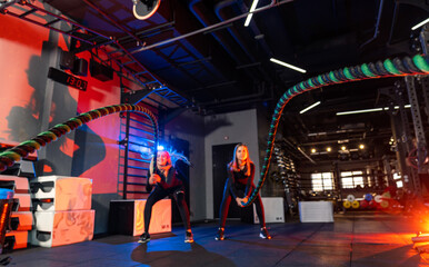 Women doing battle ropes indoors. Two women perform battle rope training in a well-equipped gym...