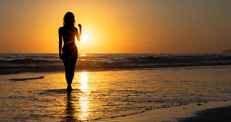Silhouette of a woman walking on the beach at sunset © Raquel