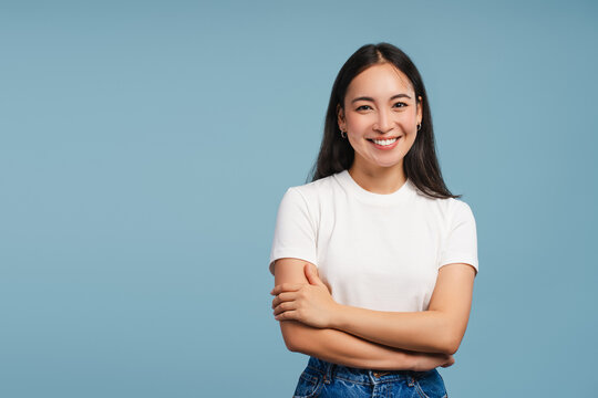 Smiling asian woman posing with crossed arms looking at camera on blue background