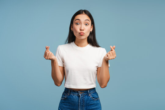 Attractive, smiling Asian woman making korean finger heart gesture on blue background