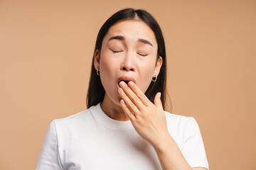 Young asian woman yawning on beige background